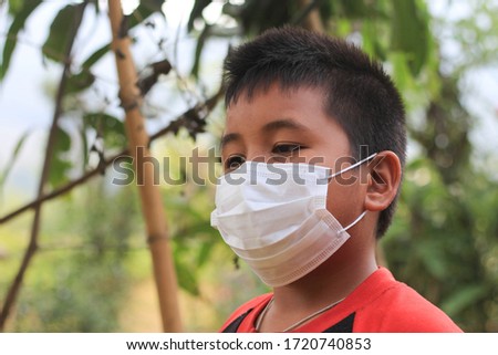 Boy wearing a protective face mask on 
nature background. A child wears a face mask during a coronavirus and flu outbreak.