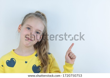 Workpiece or template with beautiful, nice, cool and pretty young girl or child in yellow T-shirt on white showing domonstrating something behind her on background by means of her hand as presentation