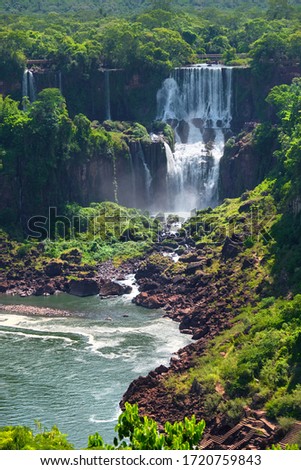 Iguazu waterfalls in Argentina, view from Devil's Mouth, close-up on powerful water streams creating mist over Iguazu river. Sub-tropical foliage in Iguasu river valley, red stone river bed.