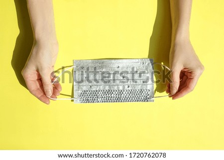 Medical mask with rhinestones in hands on yellow background. Epidemic concept, flat lay.