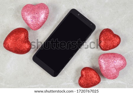 A smart phone chills romantically atop a stone background surrounded by glittery hearts.