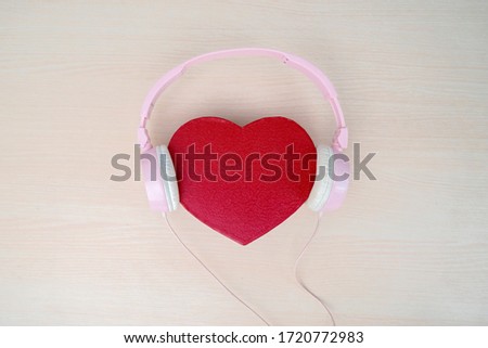 Flat layout of red heart shaped pillow, with pink headphone in wooden table background