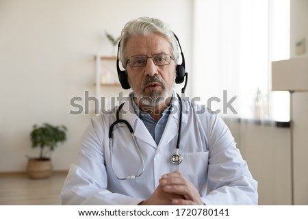 Older male doctor therapist wearing headset videoconferencing talking to web camera consulting virtual patient online by video conference call chat. Telemedicine, telehealth concept. Webcam view. Royalty-Free Stock Photo #1720780141