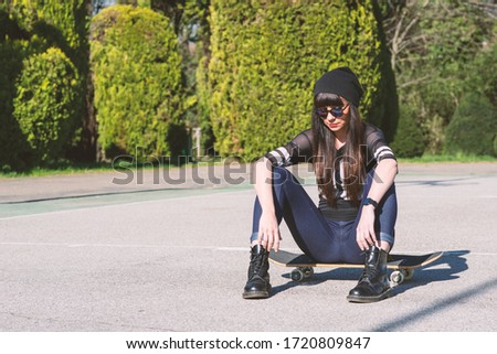 Young woman sit on skateboard outdoors in a basketball playground.