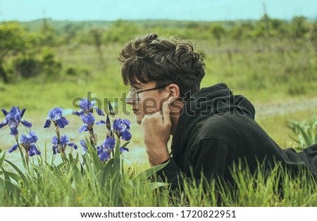 Young man with glasses admires nature, Iris flowers. Relax in nature. Pollen allergies concept.