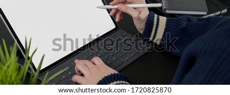 Cropped shot of female freelancer working on mock-up digital tablet with stylus pen on black table