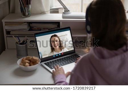 Back view of teenage girl sit at desk at home on quarantine talk on video call with mom, schoolgirl have online webcam conversation, engaged in web lesson or training with teacher or tutor on laptop