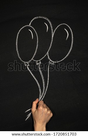 hand holds white balloons drawn in chalk on a black chalkboard