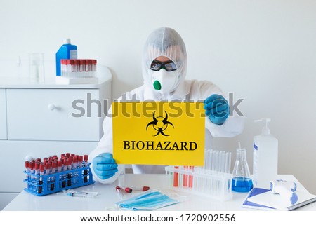 Doctor holding poster with sign Biohazard over yellow bakground. Coronavirus outbreak and pandemic concept.