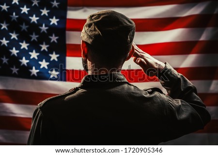 Memorial day. A uniformed soldier salutes against the background of the American flag. Rear view. Dark colors. The concept of the American national holidays and patriotism Royalty-Free Stock Photo #1720905346