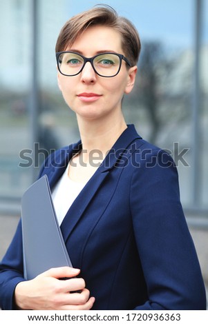 Portrait of successful cheerful businesswoman with paper documents working on organisation and creating new startup project sitting with computer in office.Young female economist posing for the camera
