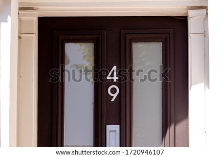 House number 49 in silver metal digits written vertically on a black wooden front door with glass inserts