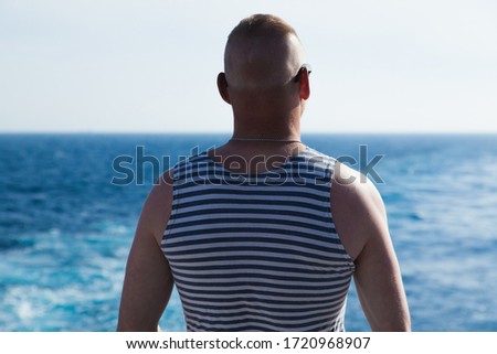 A man is a sailor from the back against the background of the sea and the sky in a striped T-shirt.