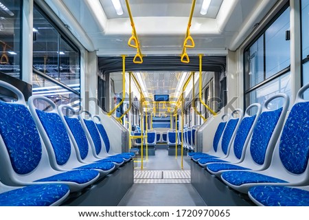 Public transport. Empty interior of the city bus. Rows of blue passenger seats and yellow handrails. The interior is equipped with handrails and hanging handles. Royalty-Free Stock Photo #1720970065