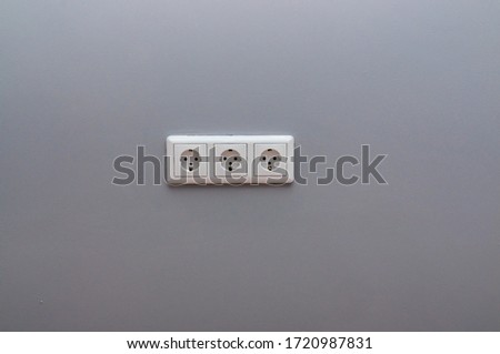 white triple socket on the gray wall.