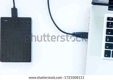 black ssd hard drive with cable connected to a laptop with white background