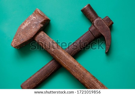 Crossed vintage hammers on a turquoise background. Two old rusty hammers on a colored background. Hand tools and labor. Place for text. Top view at an angle. Selective focus.