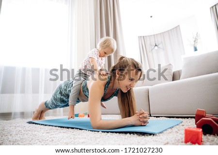 Home workout. Young attractive mom with a sports figure doing sports at home with her little cute daughter 