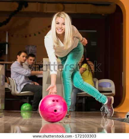 People watching young blond woman throwing bowling ball