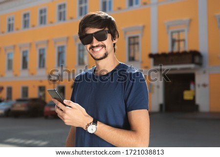 Young brunet man with beard and mustache smiling holdiing mobile phone walking down the street. Concept of communication. Being successful