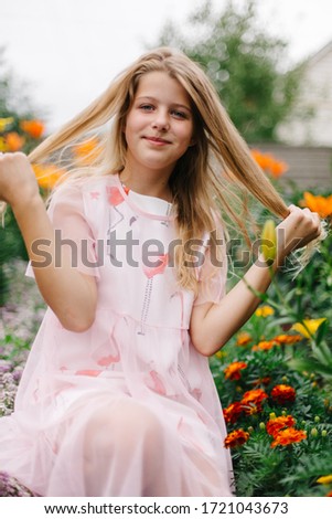 beautiful blue-eyed girl with long blond hair. little girl in a pink flamingo dress. girl in the flower garden. summer bright, emotional photo. large, thick, bright flower garden near the house. 