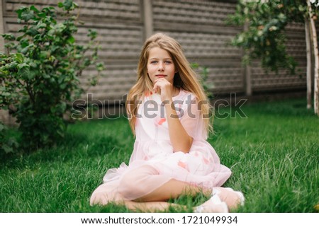 beautiful blue-eyed girl with long blond hair. little girl in a pink flamingo dress. summer bright, emotional photo.  girl model with long hair sits on green grass