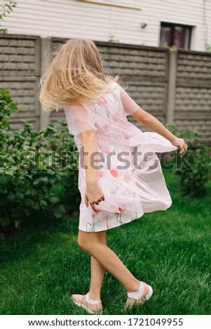 beautiful blue-eyed girl with long blond hair. little girl in a pink flamingo dress. summer bright, emotional photo.  girl model with long hair sits on green grass