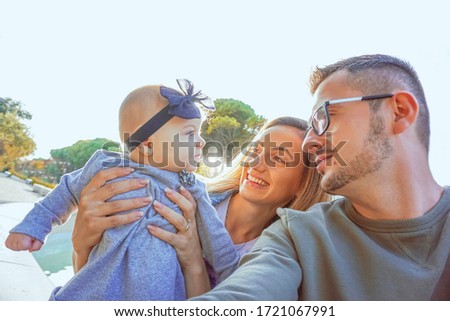 Parents holding their baby girl in arms and taking a selfie - Family picture in nature , outside in fresh air - Parenthood concept
