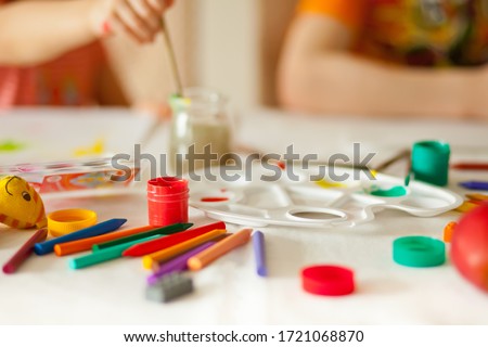 A kids drawing with colored paints on the papers. Brushes, paints, gouache and colorful pencils on the background.
