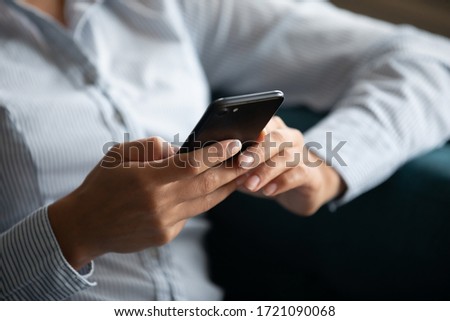 Close up focus on smartphone in female hands. Young mixed race woman using mobile applications, chatting in social networks, typing message, reading news, shopping online, ordering  food.