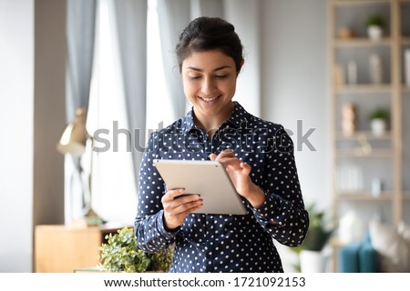 Smiling pleasant pretty indian young student girl web surfing online, chatting communicating with friends in social networks. Happy millennial hindu woman using electronic gadget digital tablet.
