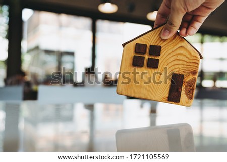 Hand choosing mini wood house model from model and row of coin money on wood table, selective focus, Planning to buy property. Choose what's the best. A symbol for construction ,ecology, loan concepts