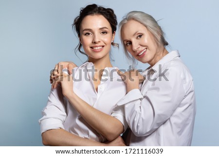 Loving senior mother hugging adorable young daughter portrait. Two beautiful woman different age wearing white shirt. Closeness and trust in family relation. Support and help from parent Royalty-Free Stock Photo #1721116039