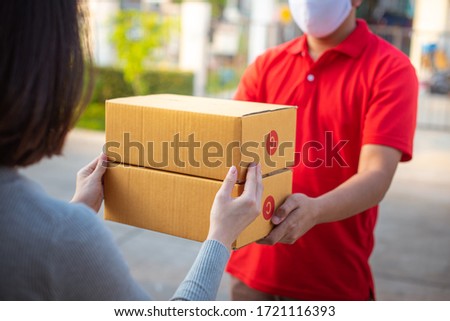 Deliver man wearing face mask in red uniform handling yellow bag of food, fruit, milk, vegetable give to female costumer Postman and express grocery delivery service during covid19. Royalty-Free Stock Photo #1721116393