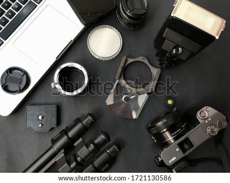 Silver computer, mirrorless reflex camera, EVIL (APSC), tripod, camera shoe, vintage lenses and adapters, flash, photo accessories on black background Royalty-Free Stock Photo #1721130586
