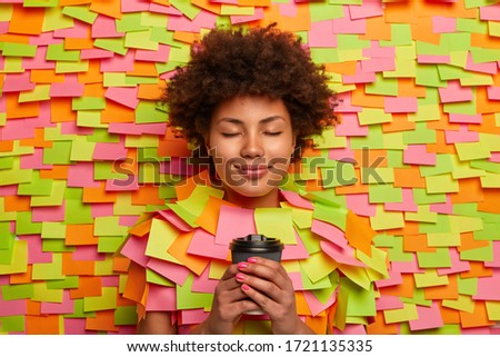 Calm relaxed woman drinks takeaway coffee, keeps eyes closed, thinks about something pleasant, enjoys drinking refreshing beverage, surrounded with colorful stickers. People, lifestyle concept