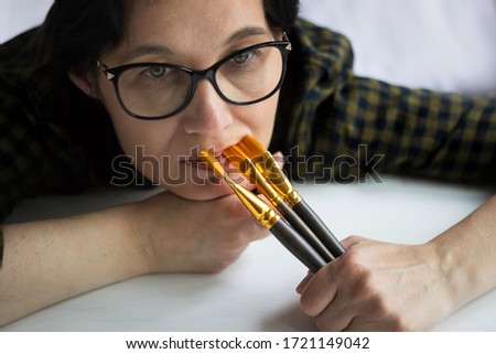 A beautiful pensive dreamy brunette with glasses is an artist with brushes in hand, looking sadly at the camera. The concept of creativity.