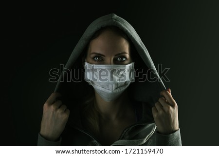 Dark photo of Young serious woman wearing medical protactive face mask and hood in the night