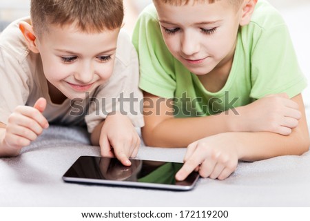 Two little smiling child boy brothers playing games or surfing internet on digital tablet computer