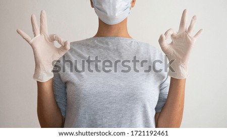 Woman with a surgical mask and latex gloves gives a OK symbol.