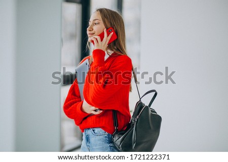 Girl student holding computer and talking on the phone by the window