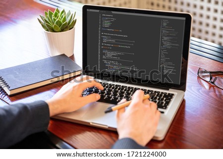 Computer code, software concept. Programmer working with a laptop, programming code on the screen, office background. Developing coding technologies.