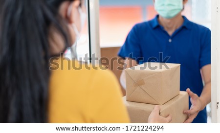 Young Asian woman wearing face mask or surgical mask signing on digital tablet for receiving package from delivery service company staff for prevent coronavirus infection during covid-19 outbreak.
