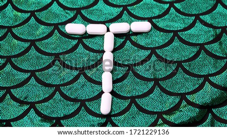 Alphabet made of pills on a green and black background. Vitamins on a background of scales. Abc from drugs. Letter T made from pills. Capital letter T of medicines