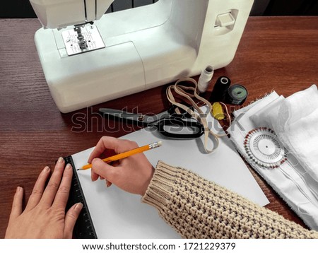 Female hands draw with a pencil and a ruler on a white sheet of paper on the background of sewing supplies. The concept of preparation for sewing, drawing a pattern
