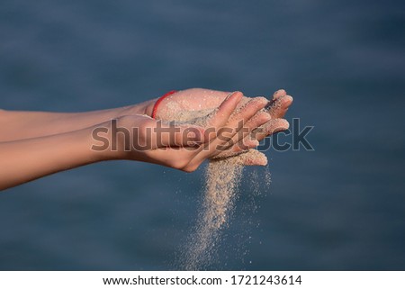 Summer beach holiday vacation concept. Hands releasing dropping sand. Sand flowing through the fingers against blue sea. Outdoor photography.