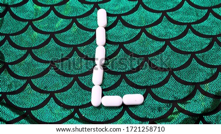 Alphabet made of pills on a green and black background. Vitamins on a background of scales. Abc from drugs. Letter L made from pills. Capital letter L of medicines