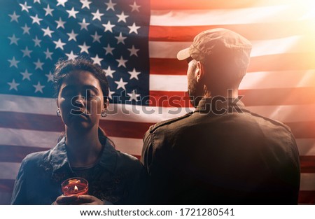 Veterans day, memorial Day. The soldier stands with his back to a woman holding a lighted candle. Couple on the background of the American flag.The concept of American national holidays and patriotism