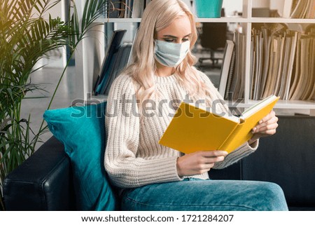 Young woman wearing protective mask on her face during coronavirus epidemic, reading a book. Lifestyle photography.