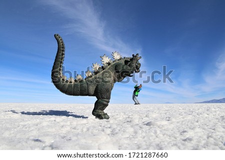 A dinosaur eating people at the Salar de Uyuni, Bolivia. Plastic dinosaur photo effect with person on salty desert.